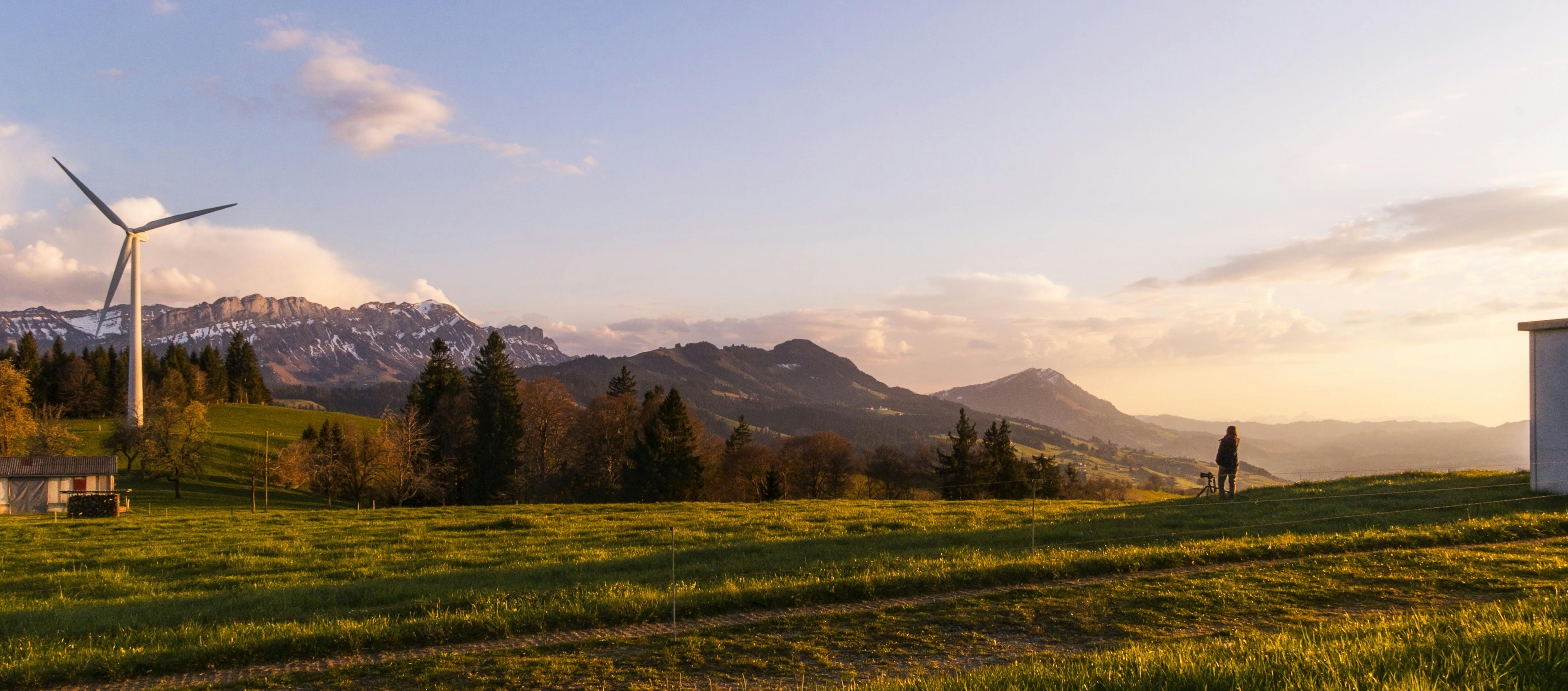 Wind turbine on an alpine hillside at sunset with a person walking